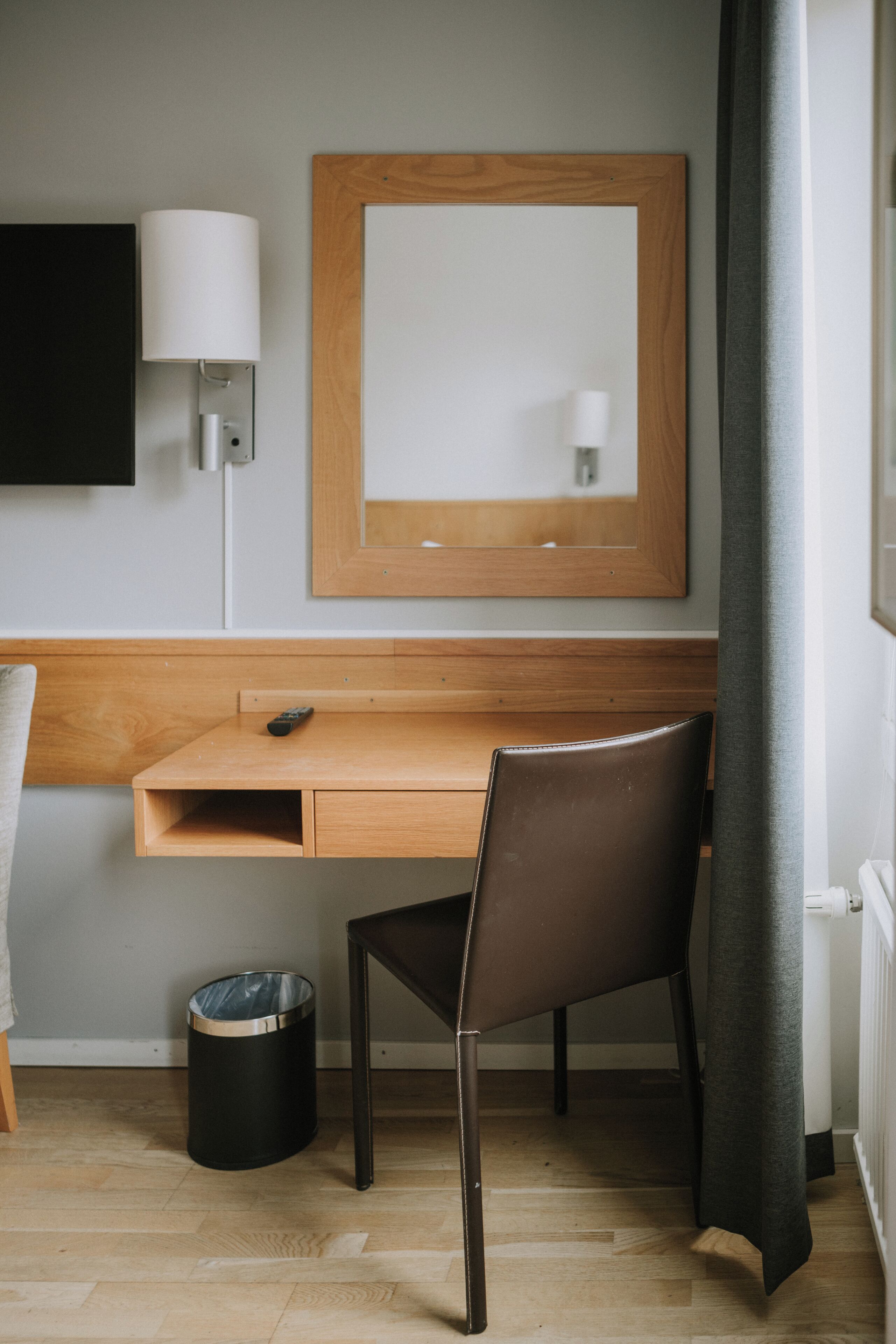 Une chambre d’hôtel avec un bureau en bois, une chaise, un téléviseur fixé au mur, un miroir et une poubelle.