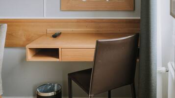 Une chambre d’hôtel avec un bureau en bois, une chaise, un téléviseur fixé au mur, un miroir et une poubelle.