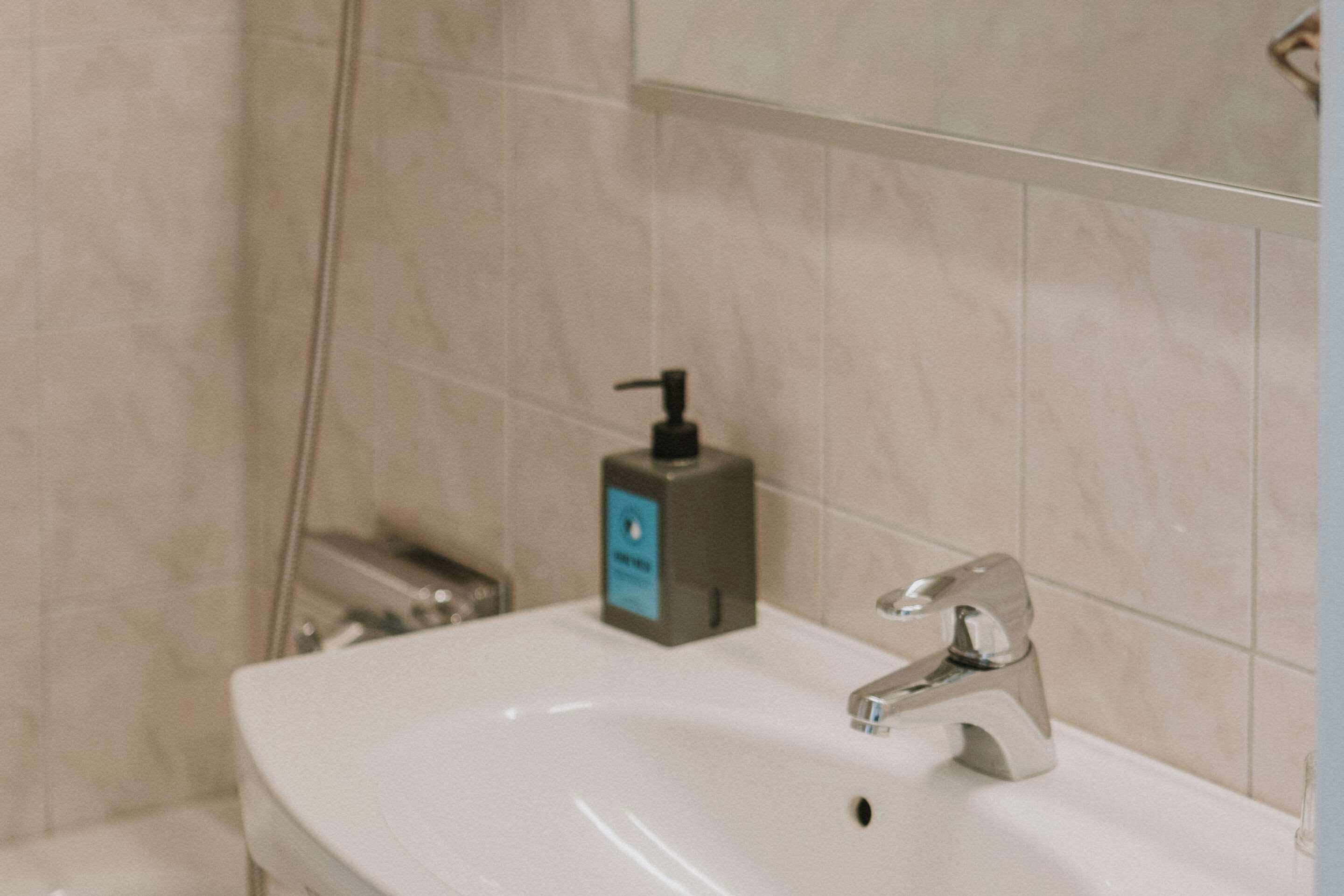 A bathroom with a white sink, a modern faucet, and a soap dispenser on the counter.