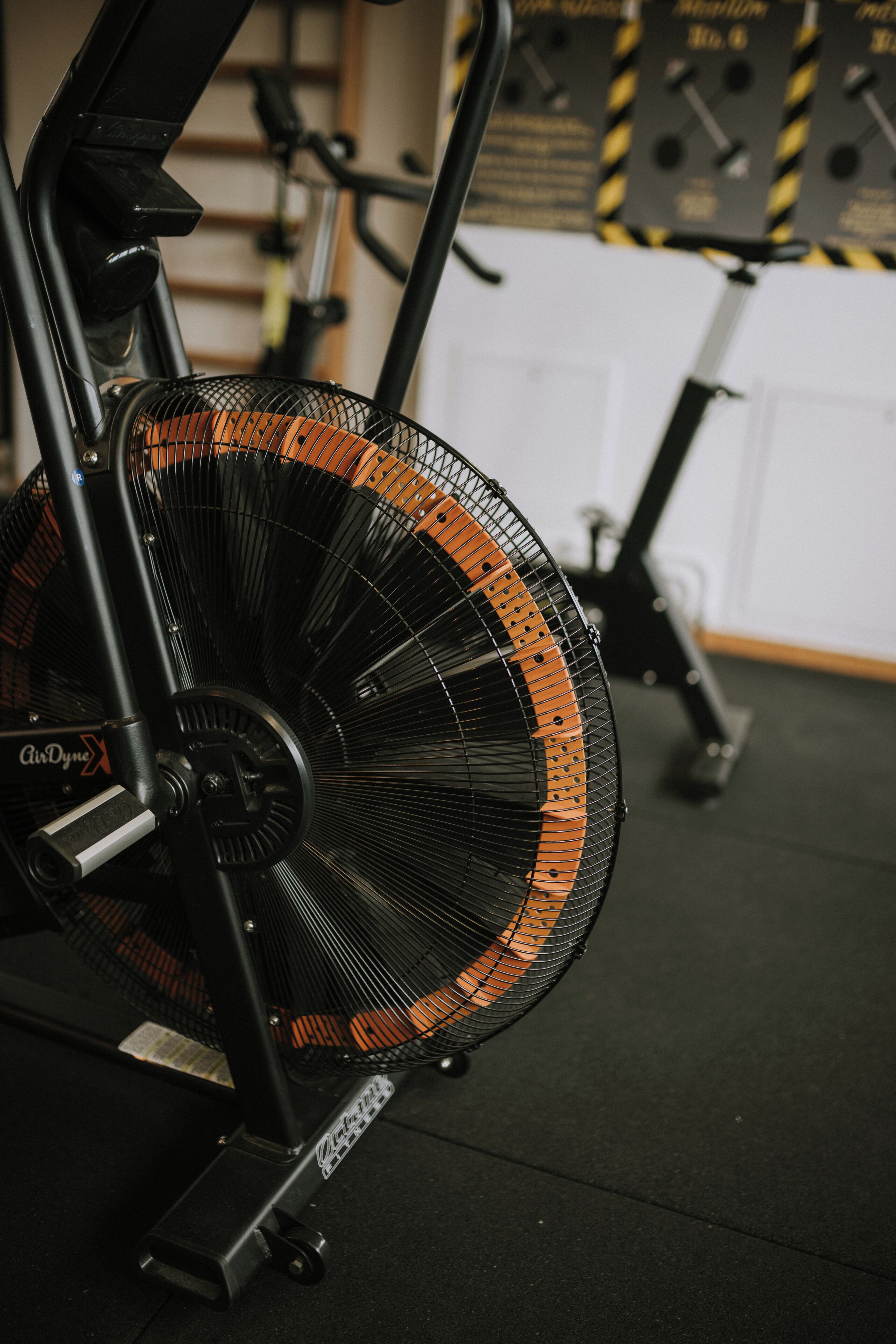 A stationary exercise bike with a fan attachment, positioned on a carpeted floor in a gym setting.