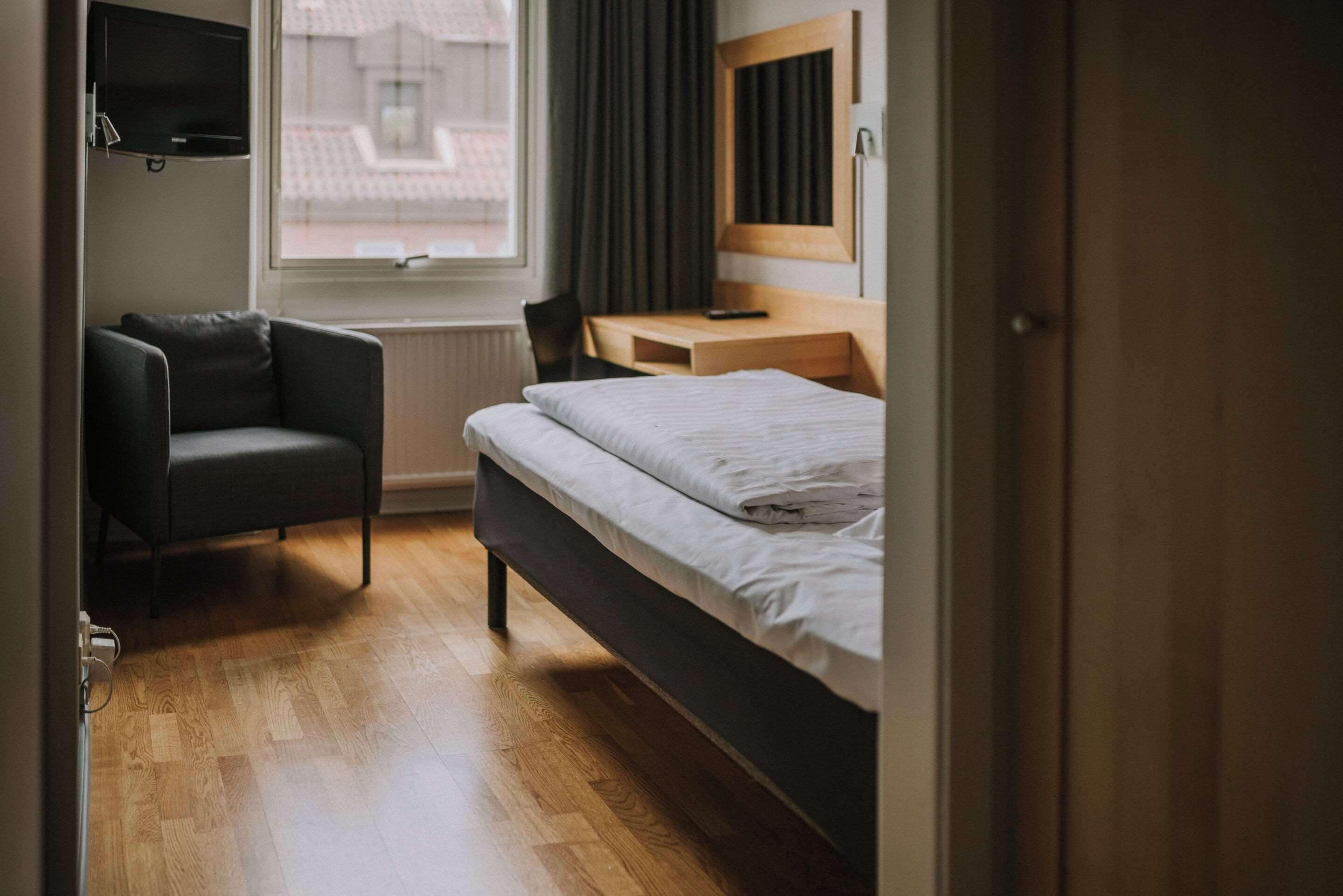 A hotel room with a bed, a desk, a chair, a TV, and a window with curtains.