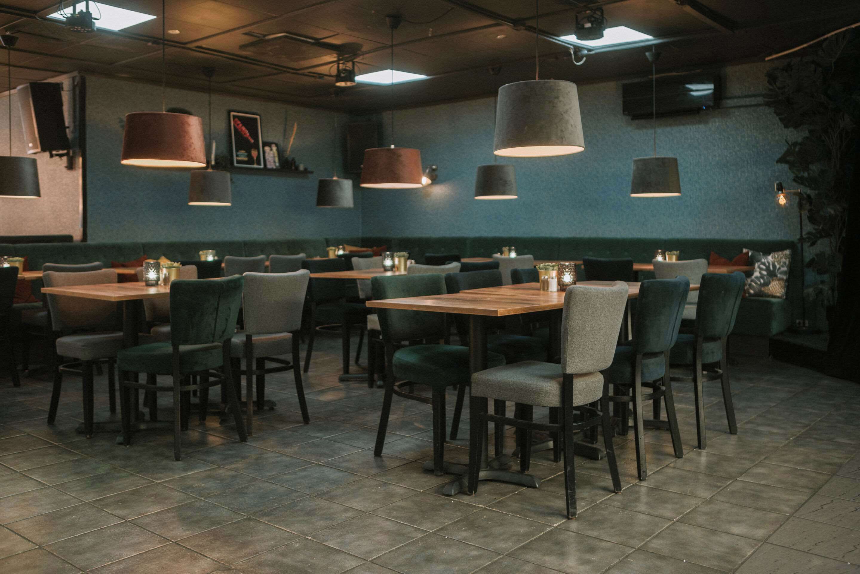 A restaurant with booths and tables, featuring pendant lighting and a tiled floor.