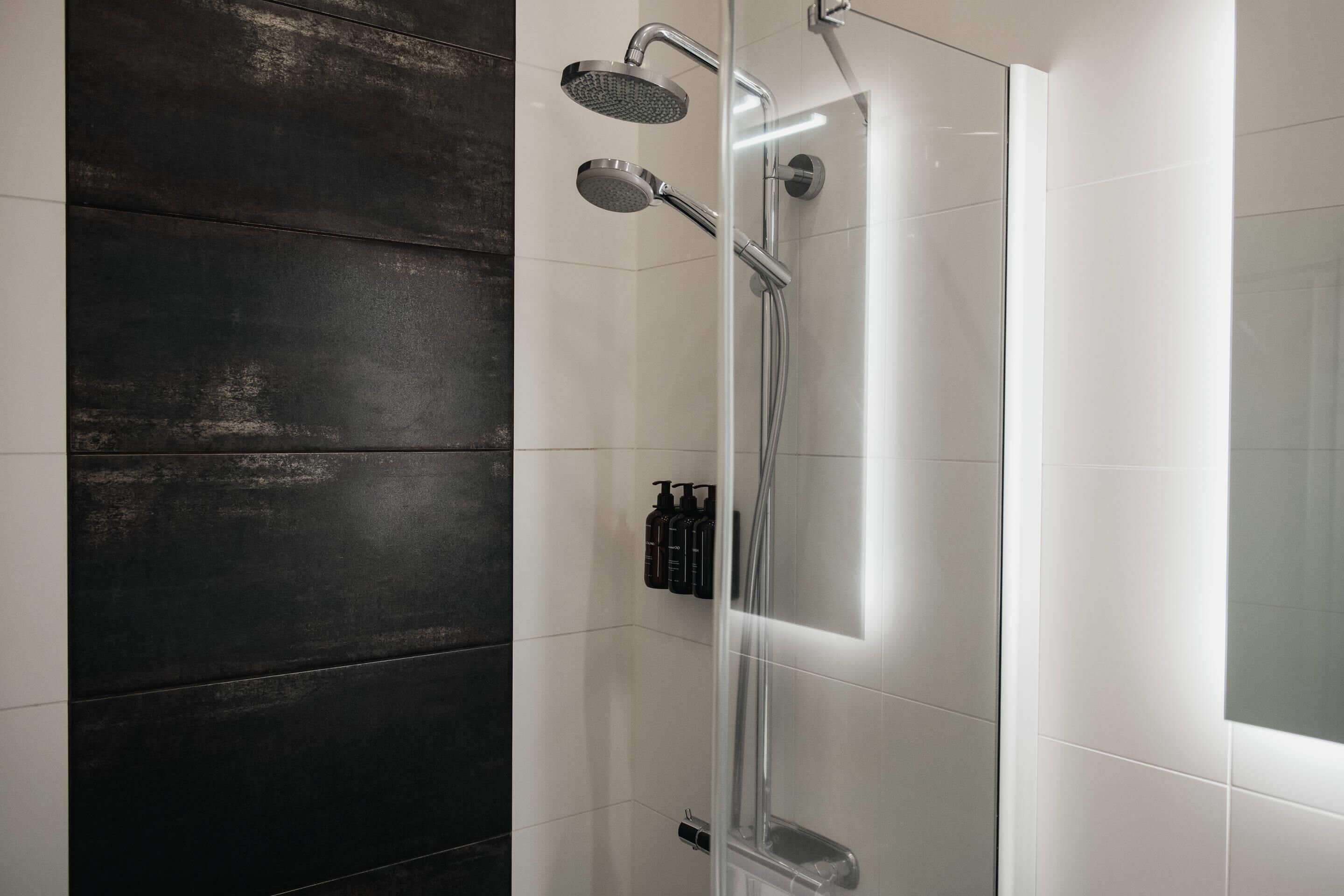 A modern shower enclosure with a glass door, a handheld showerhead, and a wall-mounted faucet.