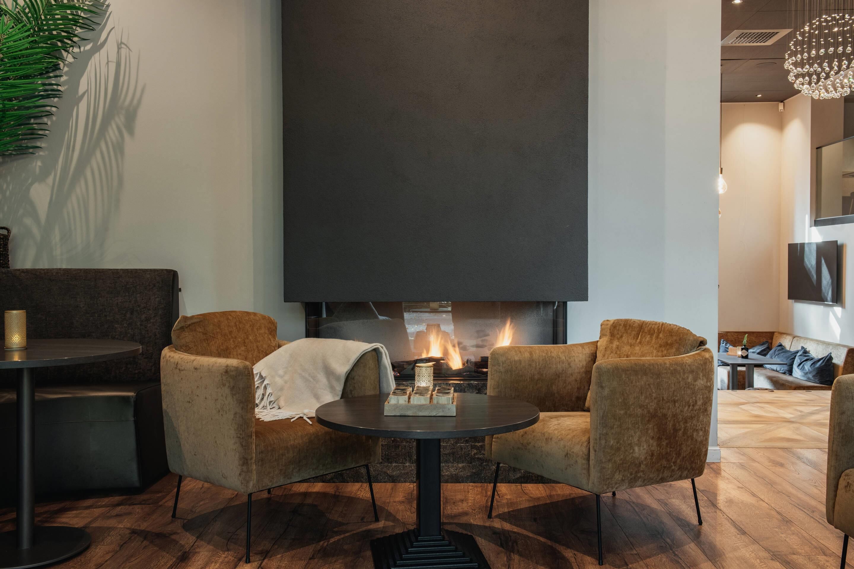 A modern living room with a fireplace, two armchairs, a round table, and a decorative plant.