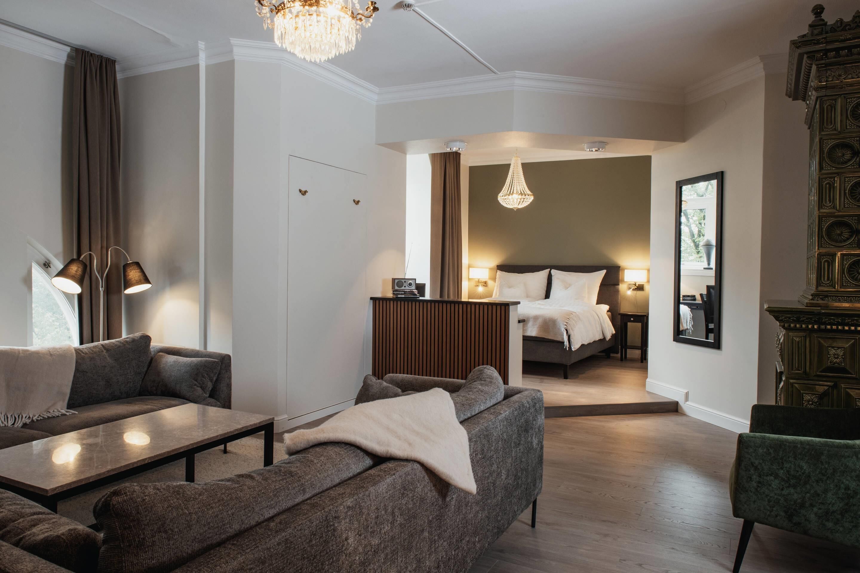 Habitació d'hotel moderna amb un sofà, una taula petita, un llit, un mirall i una làmpada penjant.