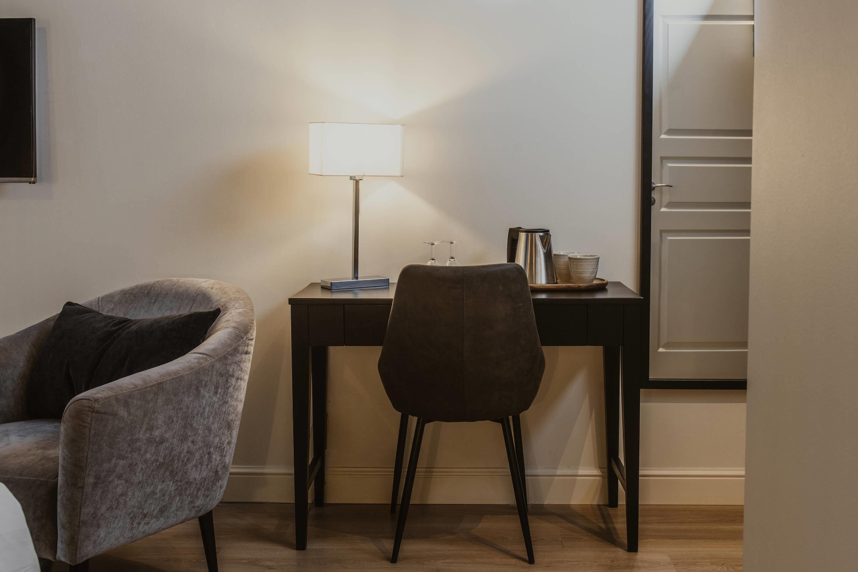 Una habitación con escritorio, silla, lámpara y puerta.