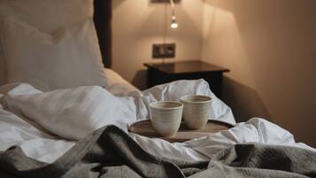 A neatly made bed with two ceramic cups on a wooden tray, a white pillow, and a bedside table with a lamp.