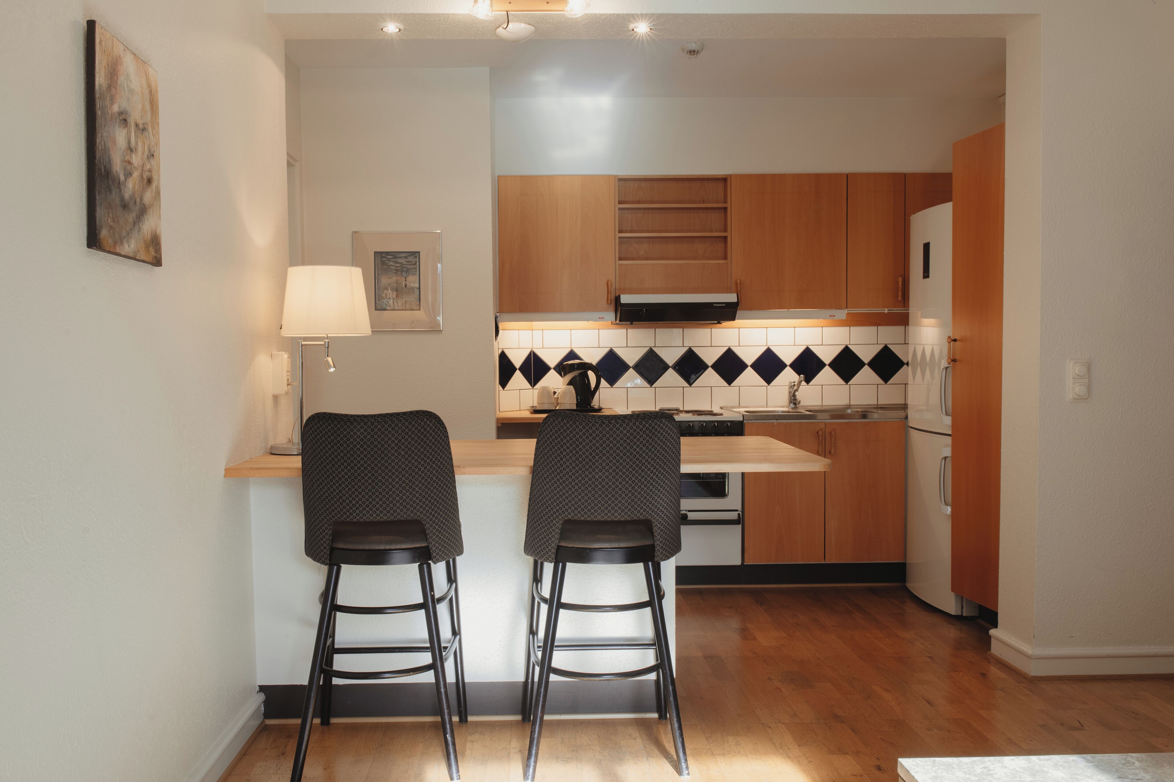A compact kitchen with wooden cabinets, a built-in oven, and two bar stools.