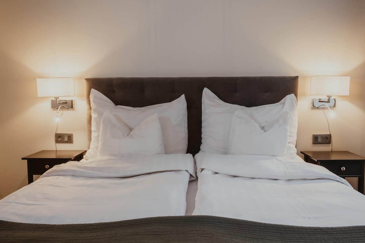 A double bed with white linens, two bedside tables with lamps, and a dark headboard.