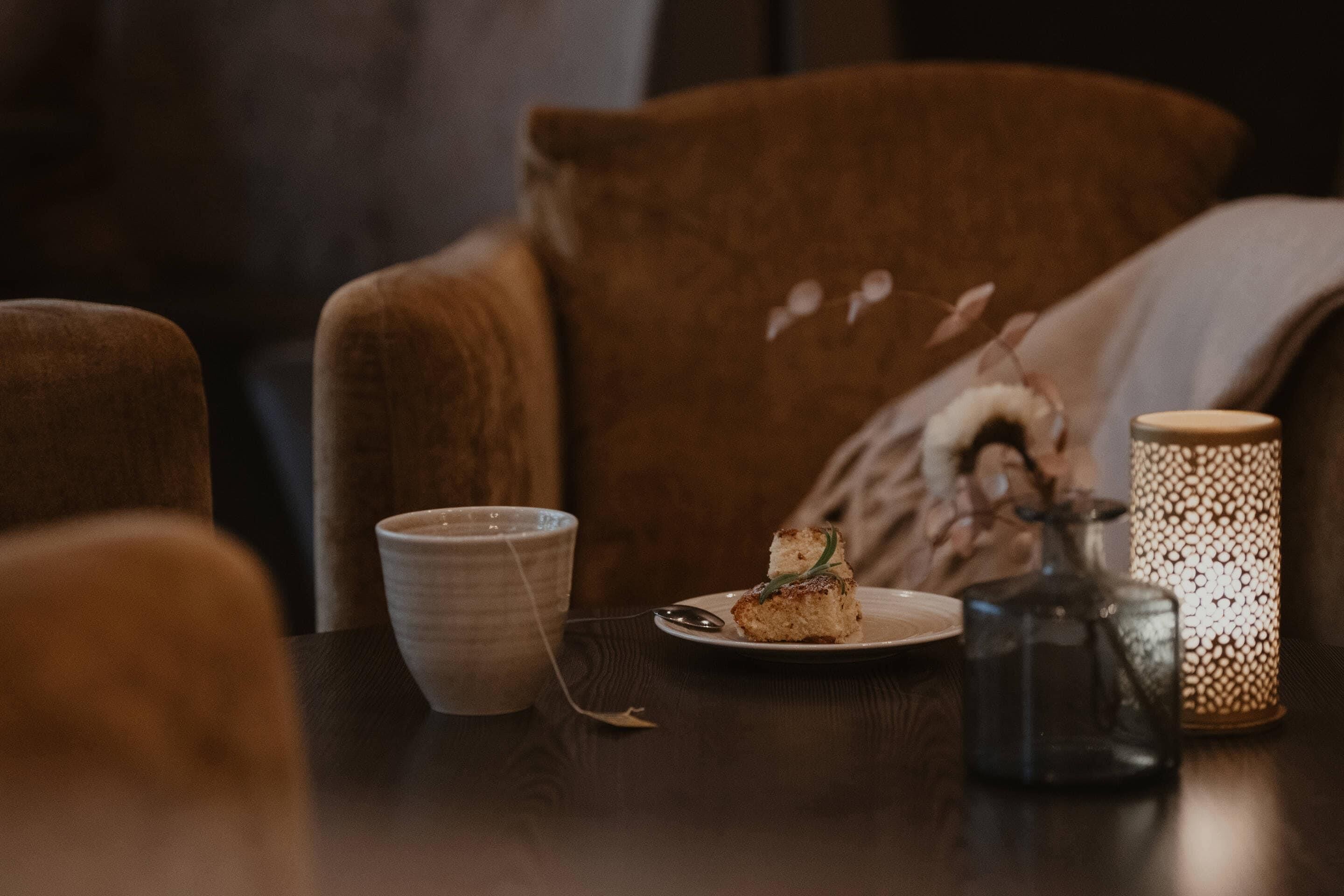 Uma mesa com uma xícara, uma fatia de bolo, uma vela e um castiçal decorativo.