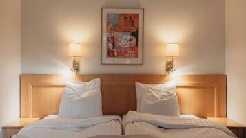 A hotel room with a wooden headboard, two bedside tables with lamps, and a framed artwork on the wall.