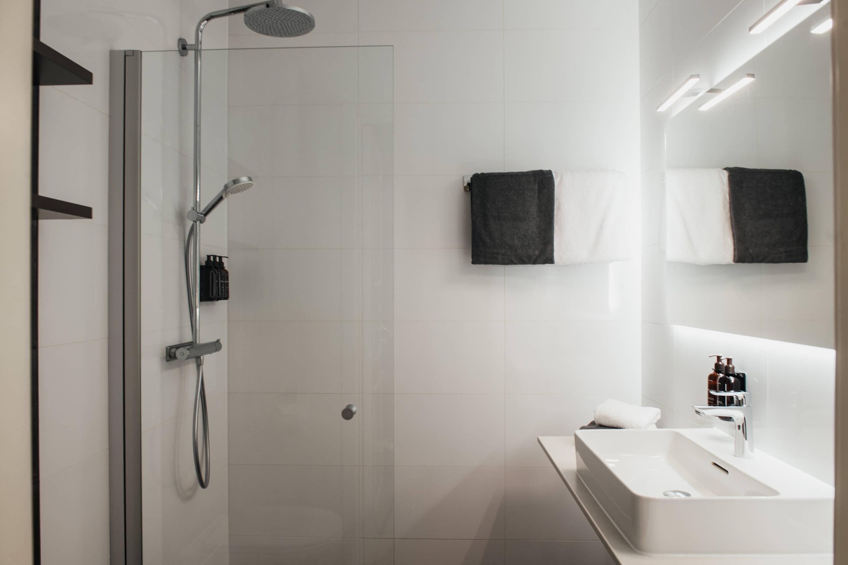 Un baño moderno con cabina de ducha de vidrio, un lavabo blanco e iluminación integrada en el espejo.
