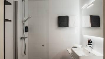 Un baño moderno con cabina de ducha de vidrio, un lavabo blanco e iluminación integrada en el espejo.