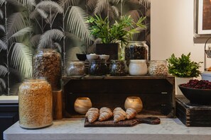 A kitchen counter with jars of grains, a plant, and croissants. - Home Hotel Norre Park (Halmstad)