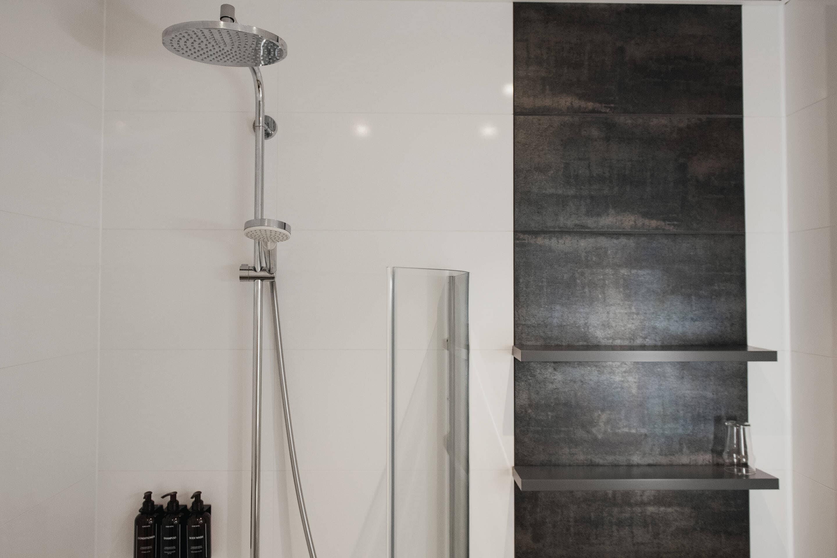 A modern bathroom with a glass-enclosed shower, a dark textured wall, and a minimalist shelf unit.