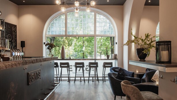 Un área de bar moderna con un amplio ventanal arqueado, taburetes y una zona de estar con un sofá y sillones.