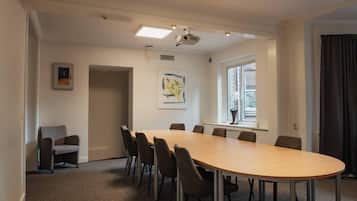 A conference room with a long table, chairs, a projector, and a window with curtains.