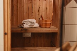 A wooden sauna with a bench, a towel stack, and a wooden bucket with a brush. - Home Hotel Norre Park (Halmstad)