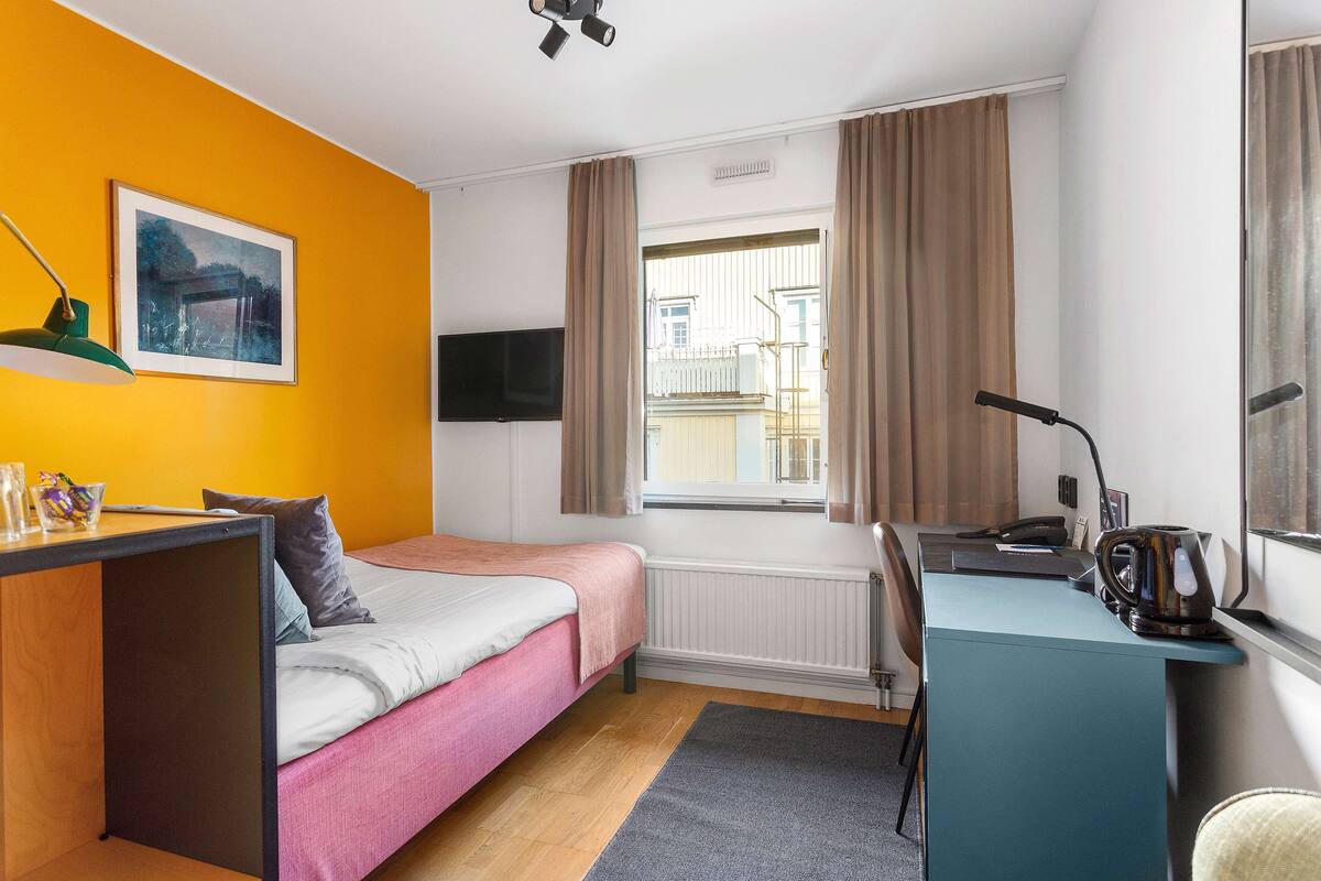Une chambre d’hôtel avec un lit, un bureau, une chaise et une fenêtre avec des rideaux.