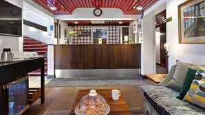 Un hall d’hôtel moderne avec un plafond en bois, un comptoir d’accueil, un canapé et une table basse sur laquelle sont disposées des pâtisseries.