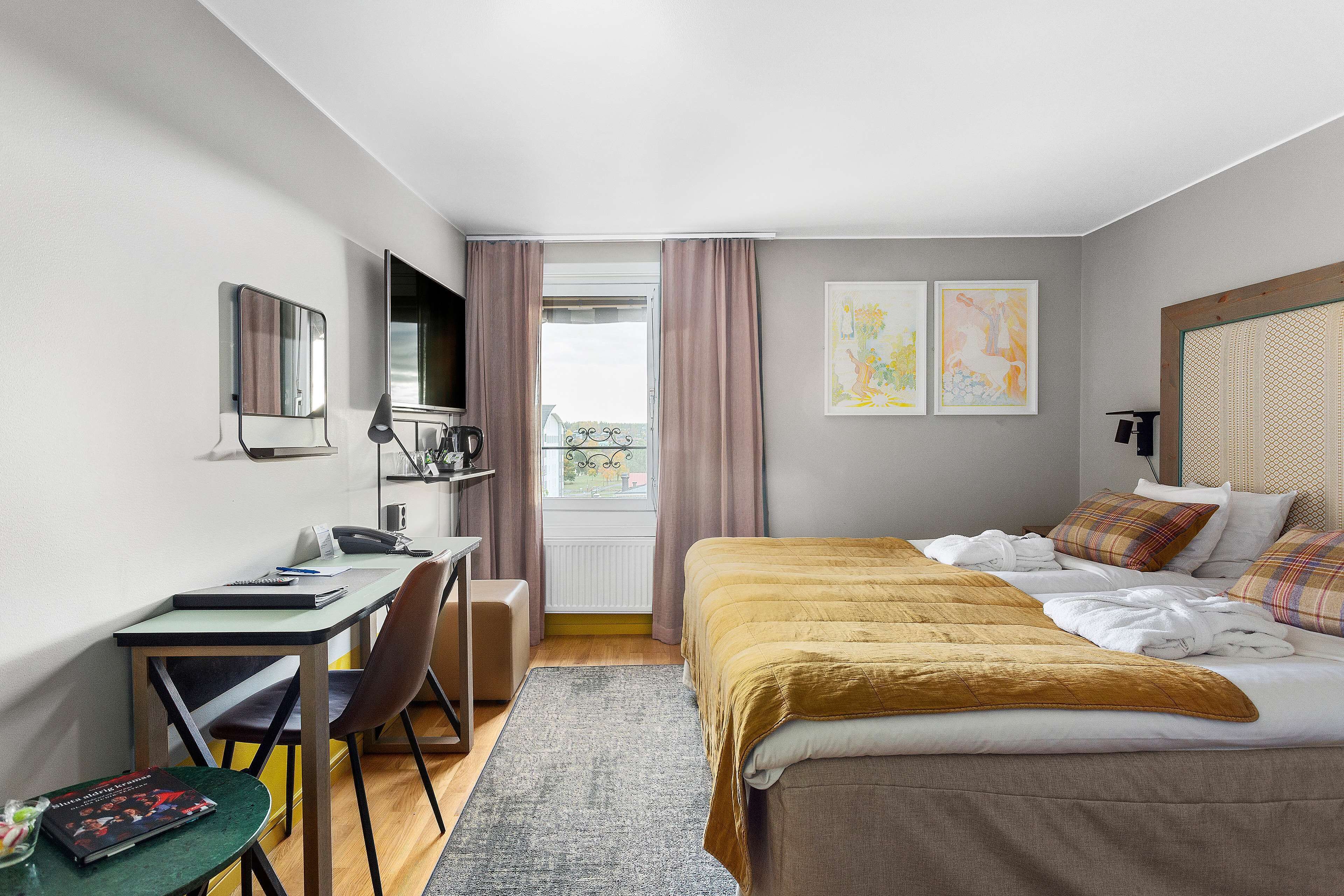Ein modernes Hotelzimmer mit Bett, Schreibtisch, Stuhl und Blick ins Freie durch ein Fenster.