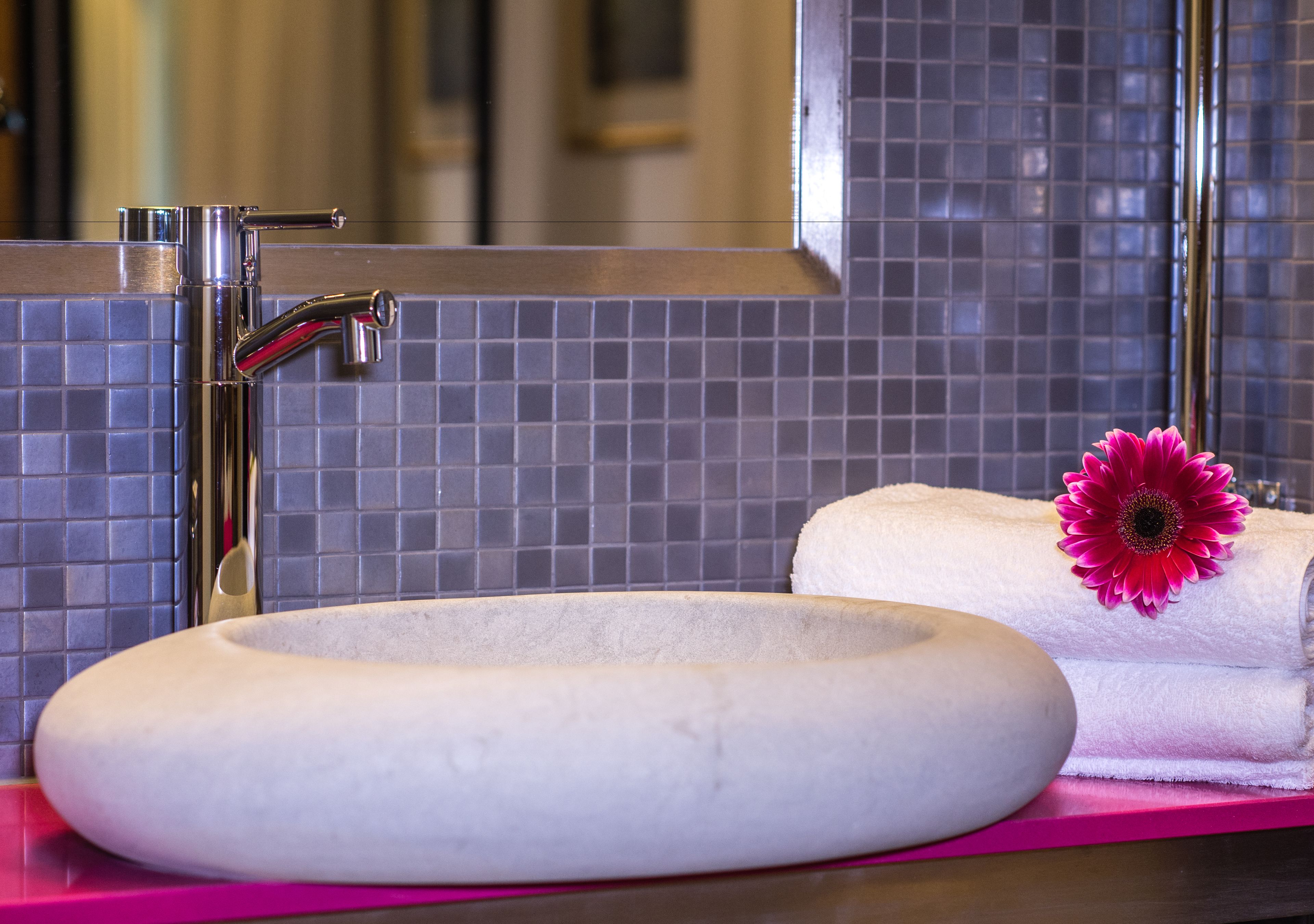 A bathroom with a round sink, a mirror, and a towel with a flower.