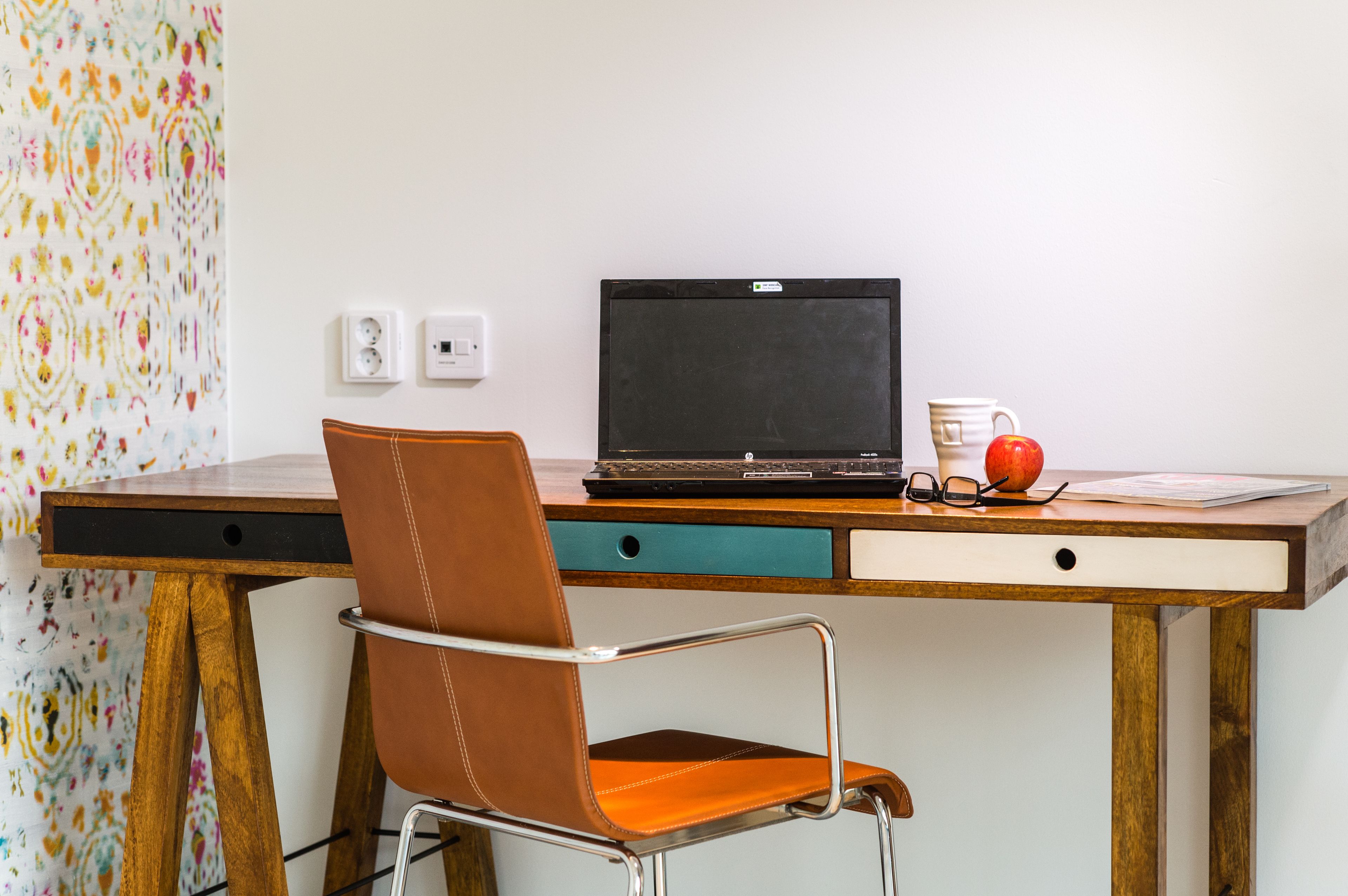 A desk with a laptop, a chair, a mug, and an apple.