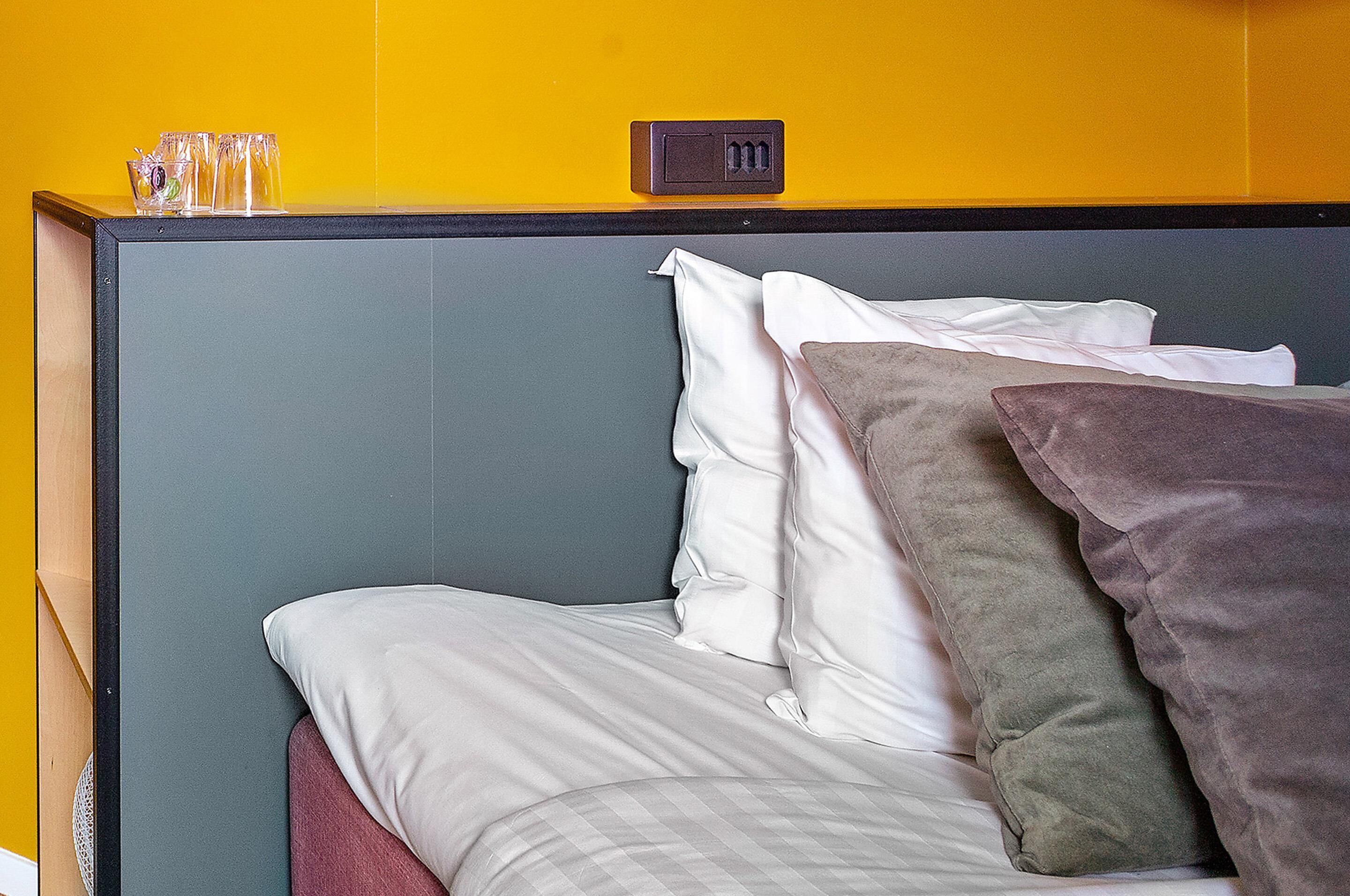 A bed with white and grey bedding, a grey headboard, and a yellow wall.