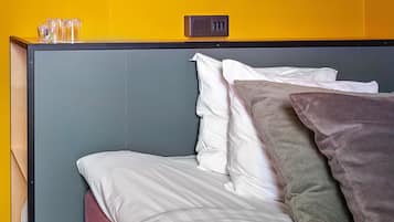 A bed with white and grey bedding, a grey headboard, and a yellow wall.