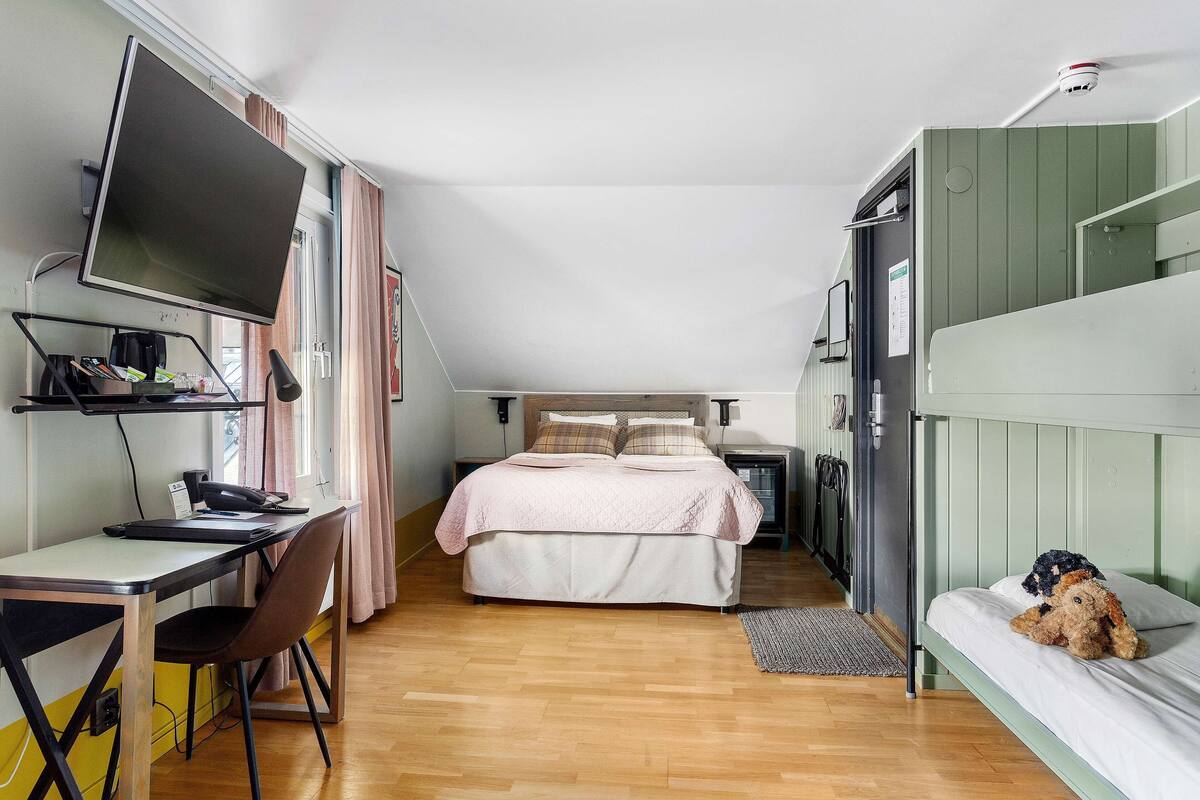 Une petite pièce comprenant un lit, un bureau avec un ordinateur, une chaise et une petite table.
