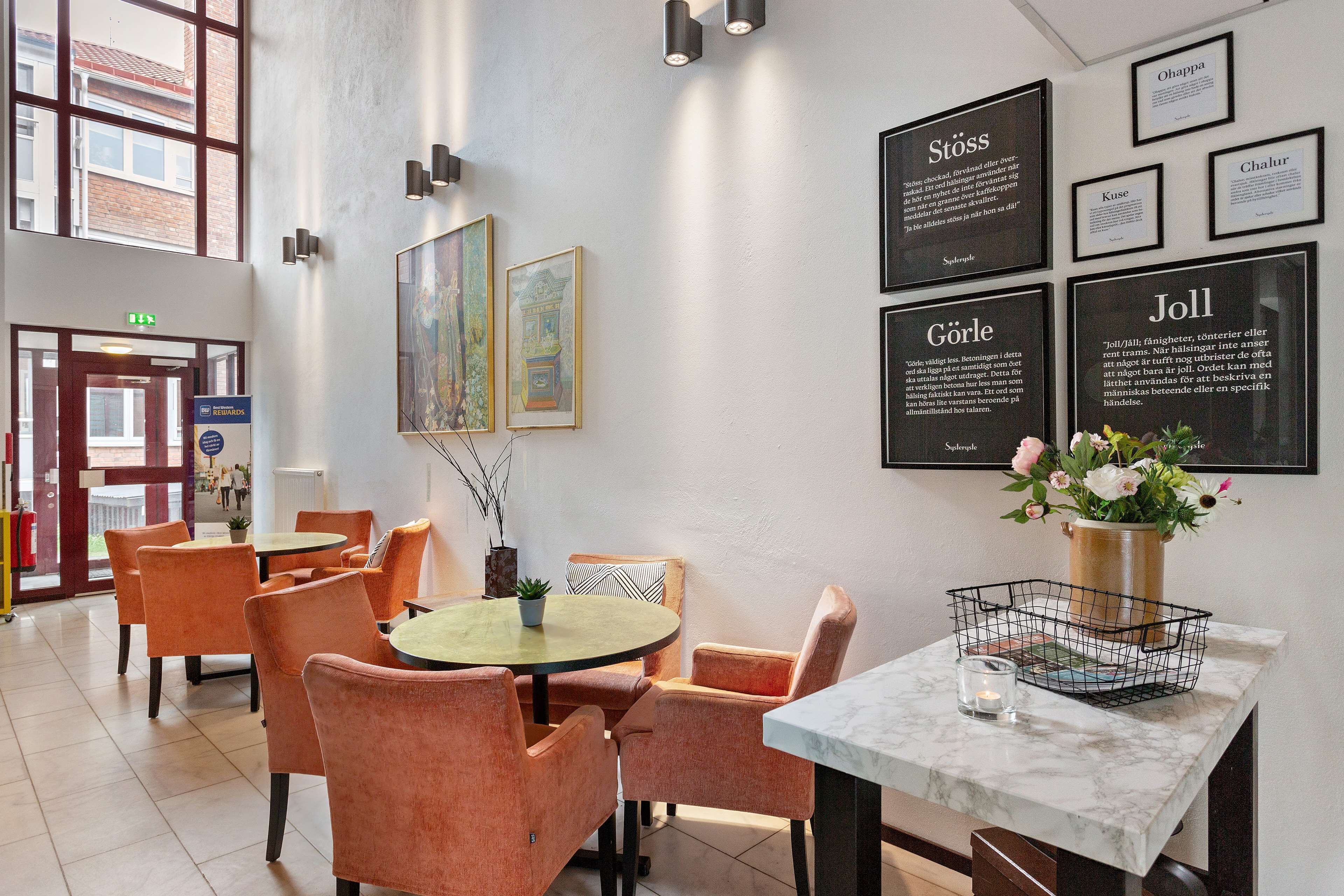 A hotel lobby with orange chairs, a round table, and a marble table with a vase of flowers.