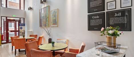 A hotel lobby with orange chairs, a round table, and a marble table with a vase of flowers.