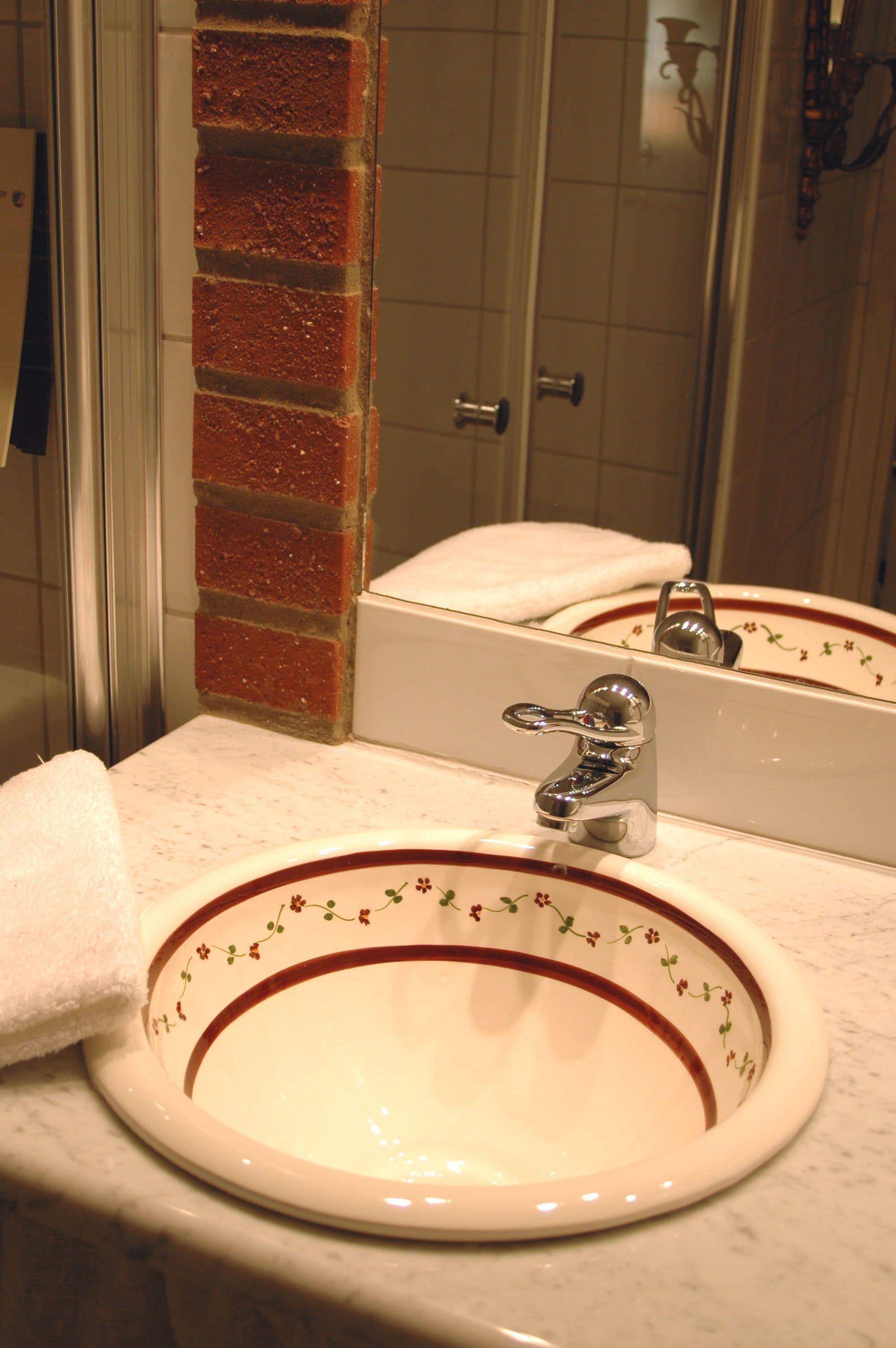 Un baño con un lavabo blanco, un espejo y una pared de ladrillo rojo.