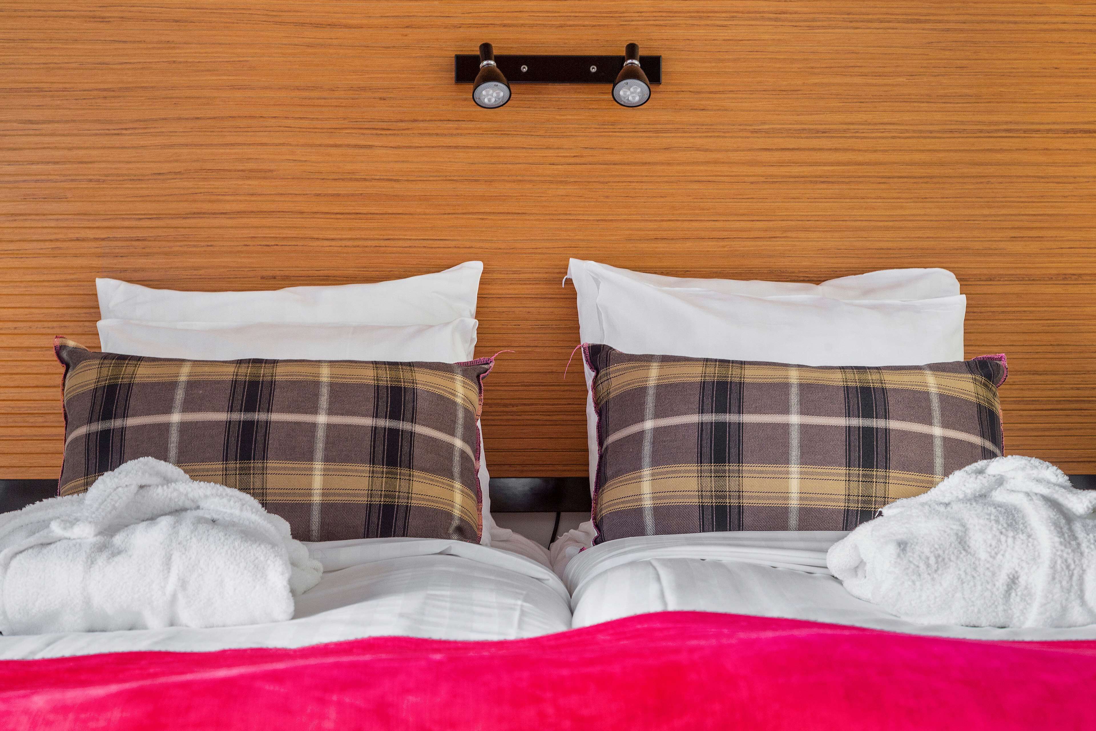 Una cama bien hecha con sábanas blancas, dos almohadas de cuadros y dos toallas blancas.
