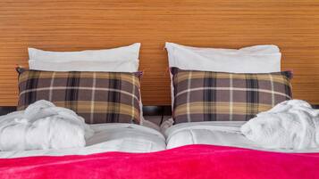 Una cama bien hecha con sábanas blancas, dos almohadas de cuadros y dos toallas blancas.