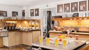 Un área de desayuno de hotel con barra de buffet, que incluye diferentes alimentos y bebidas.