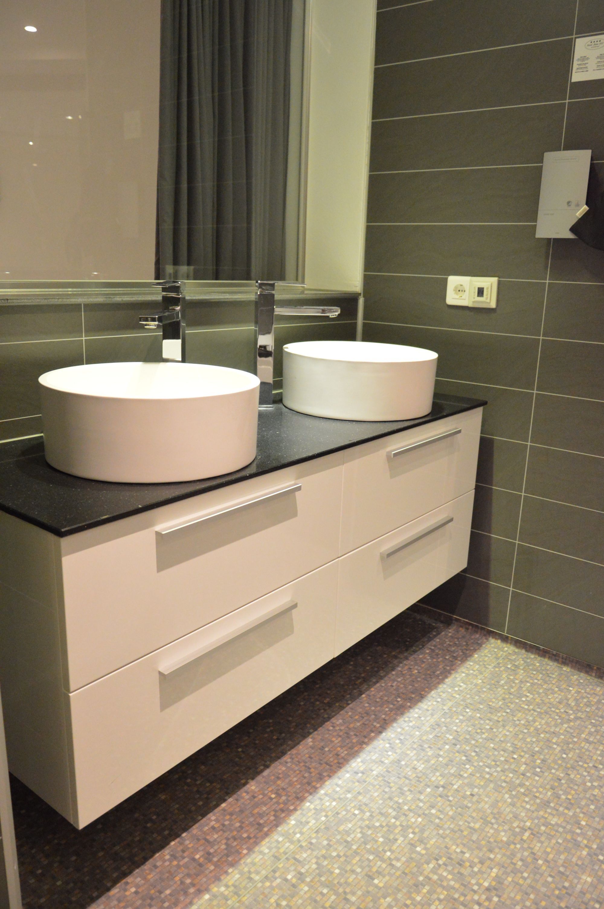 Un bagno moderno con due lavabi bianchi rotondi, un piano di lavoro nero e uno specchio soprastante.