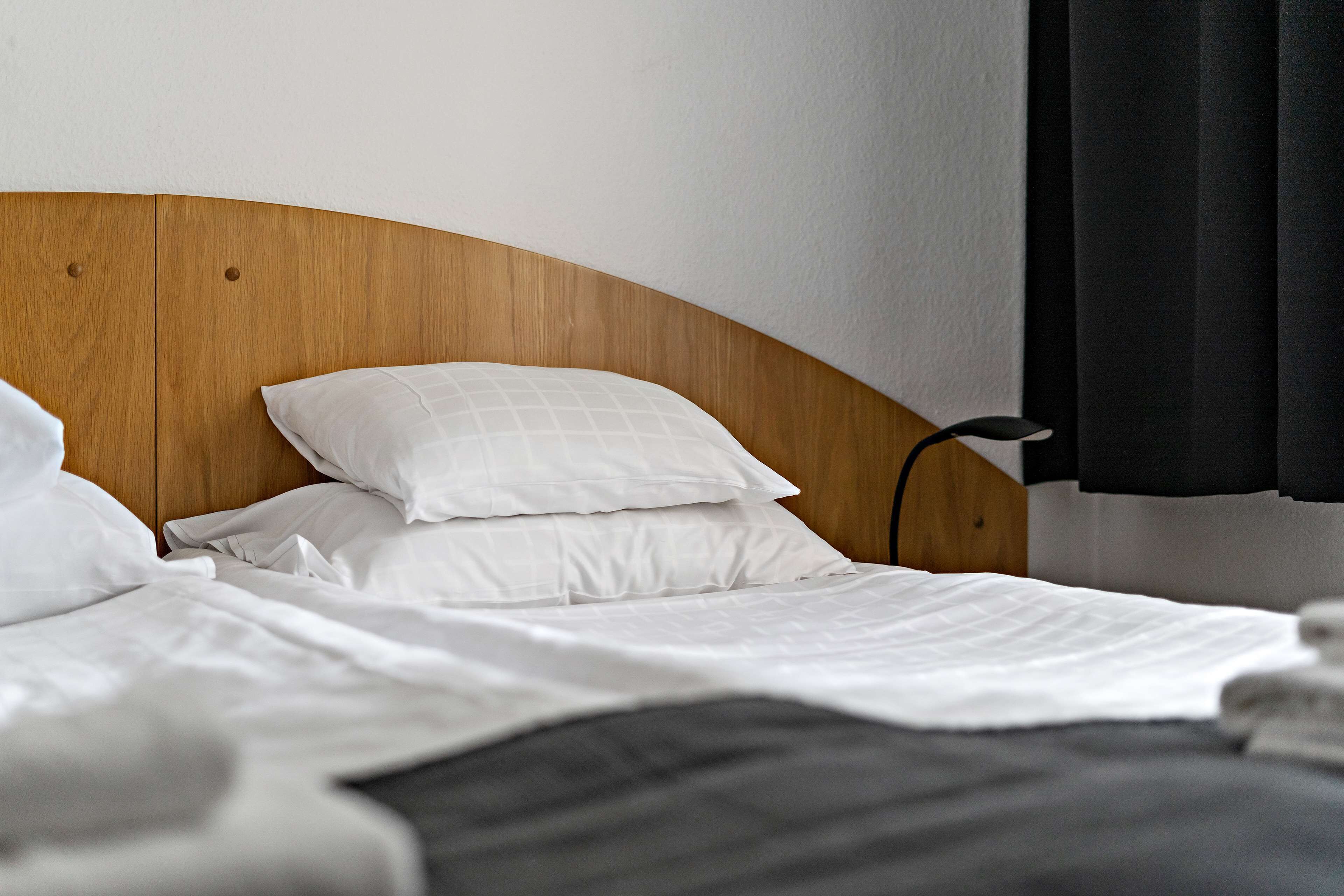 Una cama bien hecha con ropa blanca y cabecera de madera.