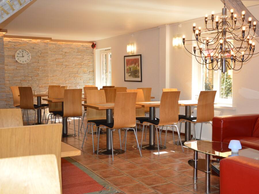 A dining area with multiple wooden tables and chairs, a red couch, a chandelier, and a clock on the wall.