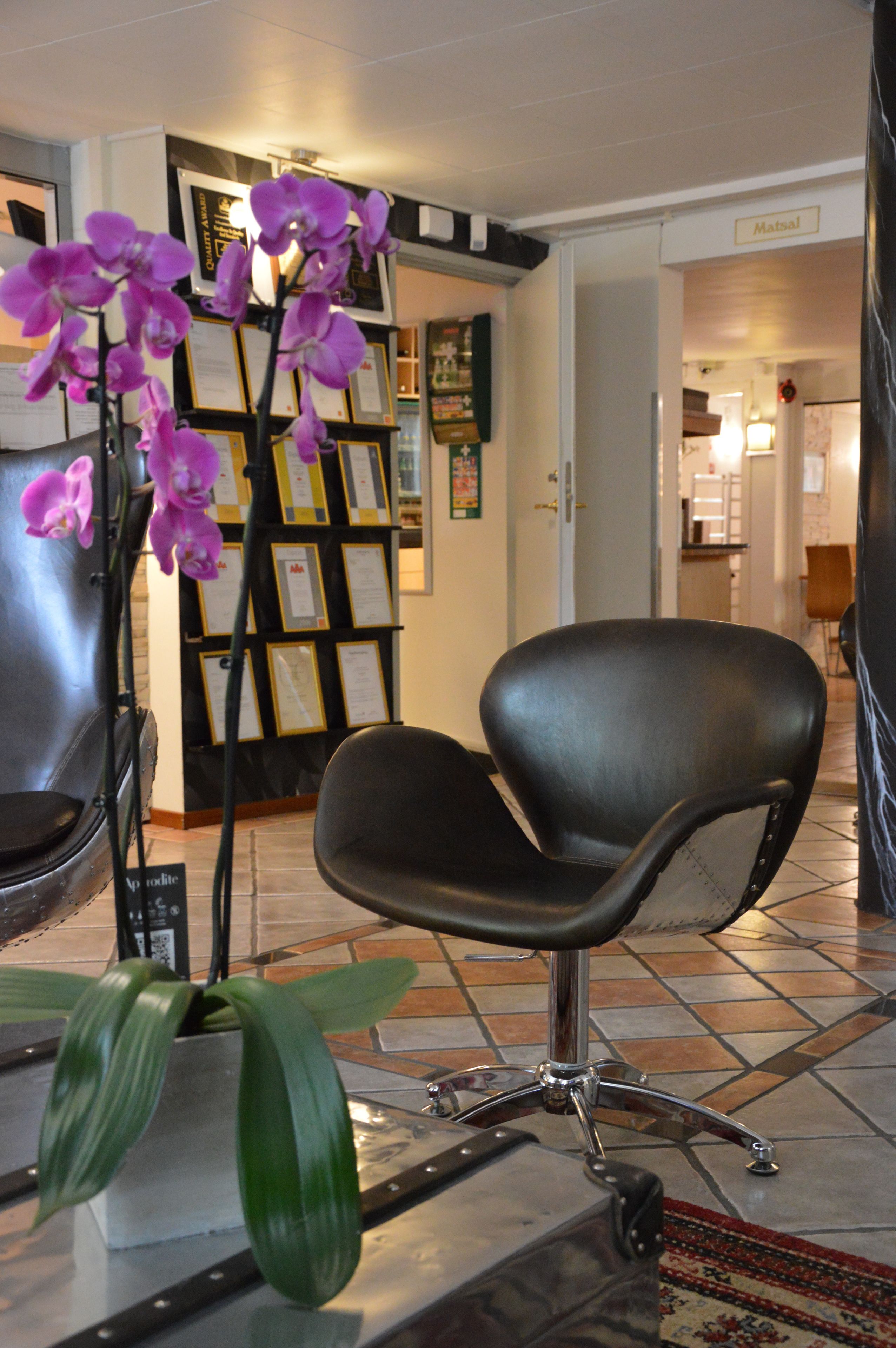 A waiting area with a black leather chair, a potted orchid, and a bulletin board with framed notices.