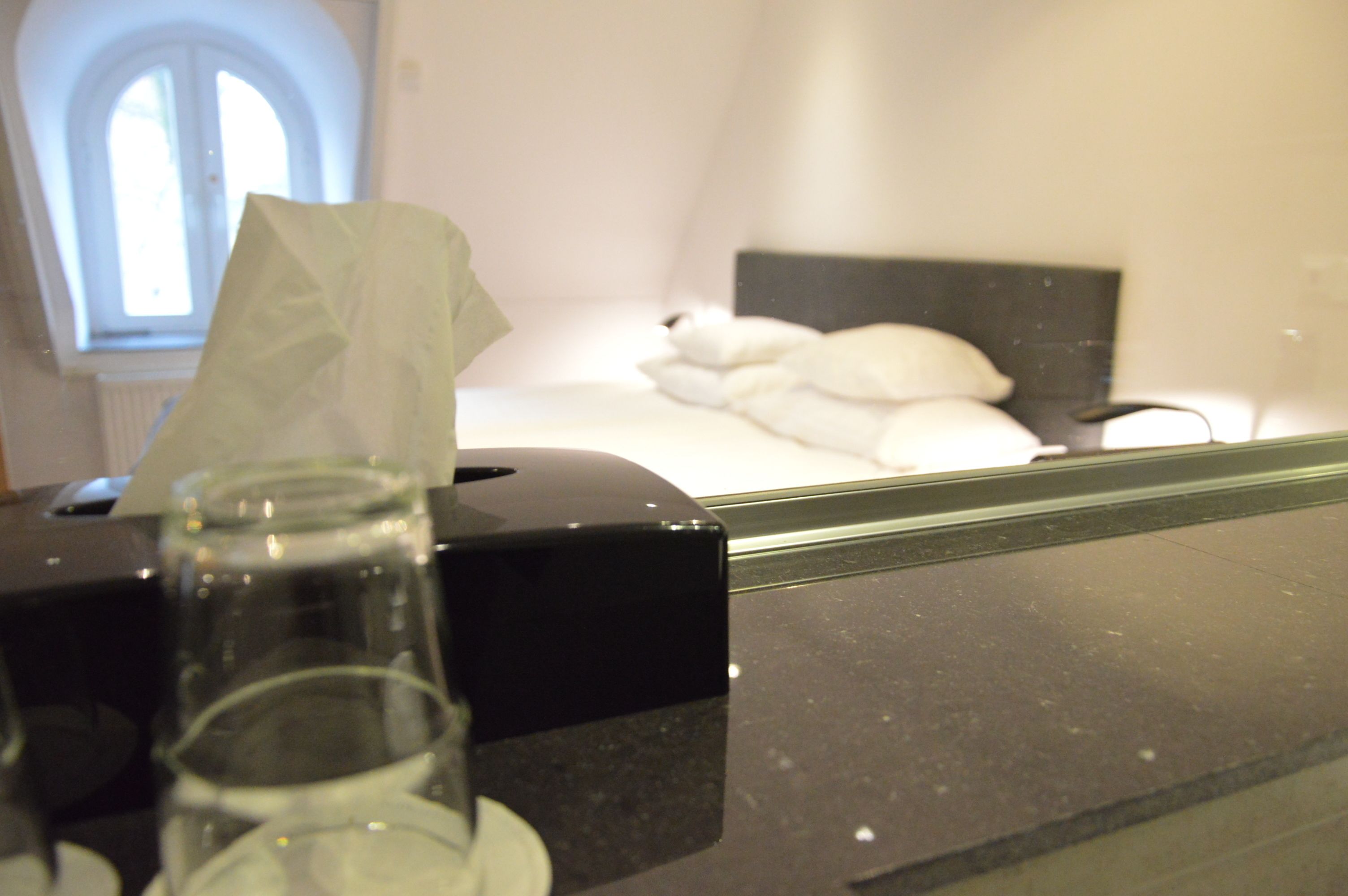 Una habitación de hotel con una cama, una mesita de noche, una caja de pañuelos y un vaso de agua.