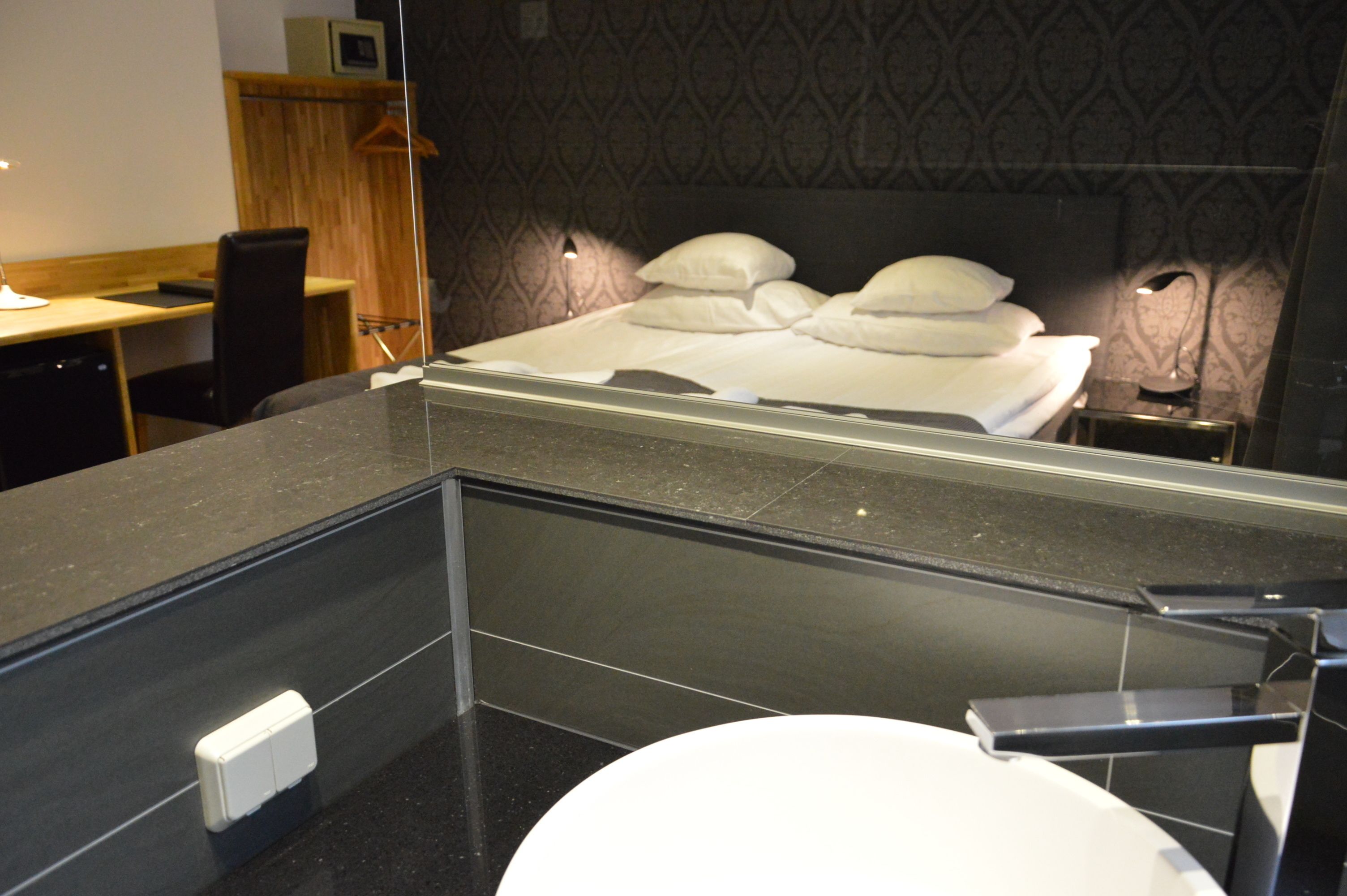 A modern bathroom with a large mirror, a toilet, and a bed with white linens.