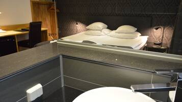 A modern bathroom with a large mirror, a toilet, and a bed with white linens.