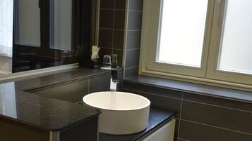 A modern bathroom with a white sink, dark tiles, and a window providing natural light.
