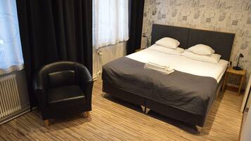 A hotel room with a bed, a chair, and a radiator.