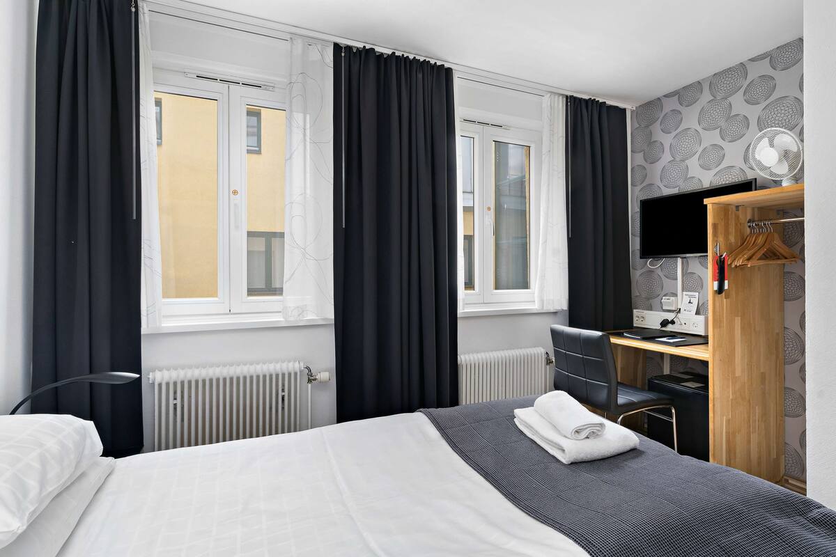 Quarto de hotel com cama, escrivaninha, cadeira, televisão e radiador.