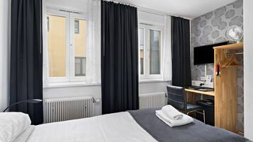 Una habitación de hotel con cama, escritorio, silla, televisor y radiador.