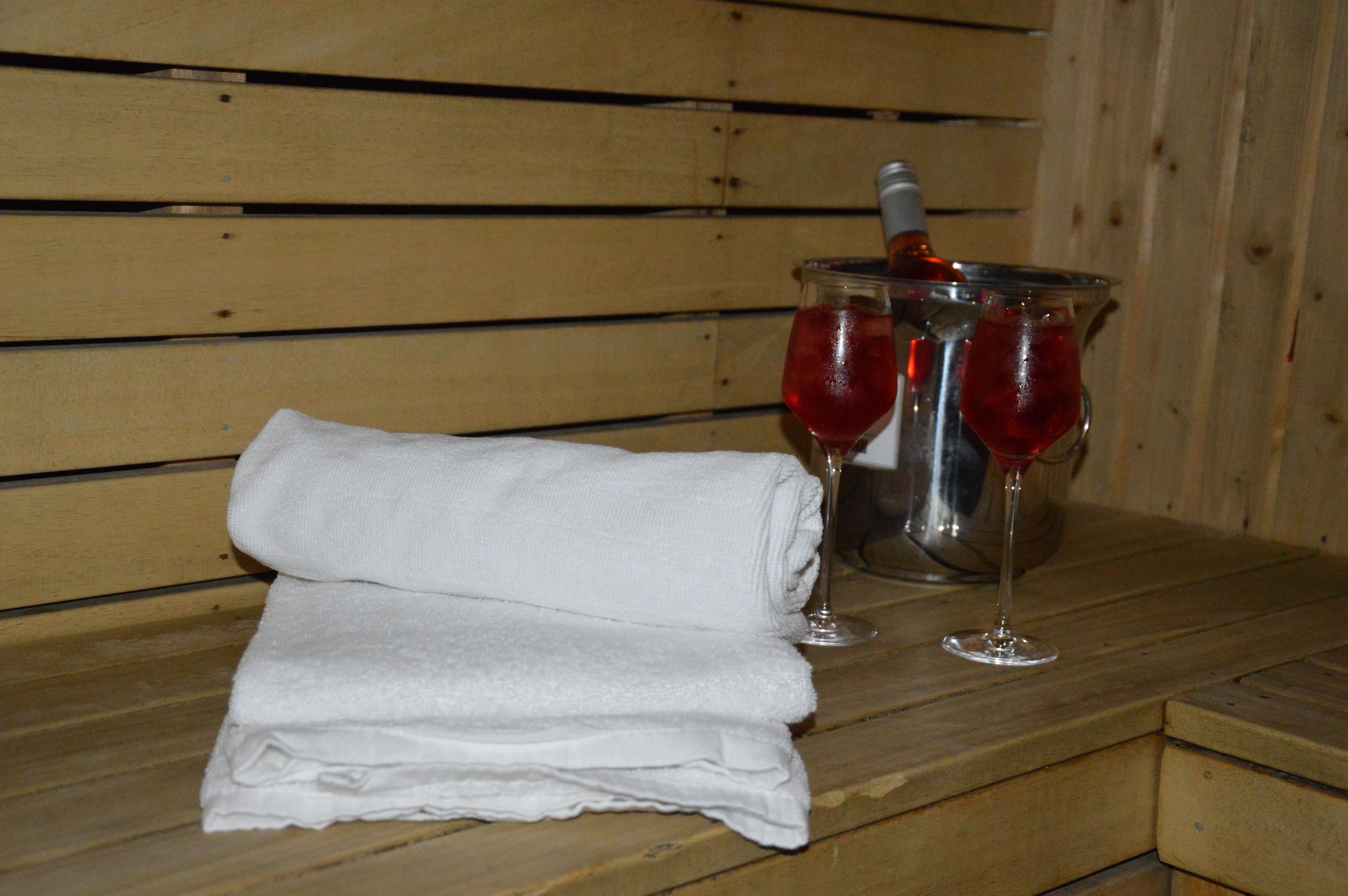 A wooden bench with a folded white towel and two glasses of red wine in a metal container.