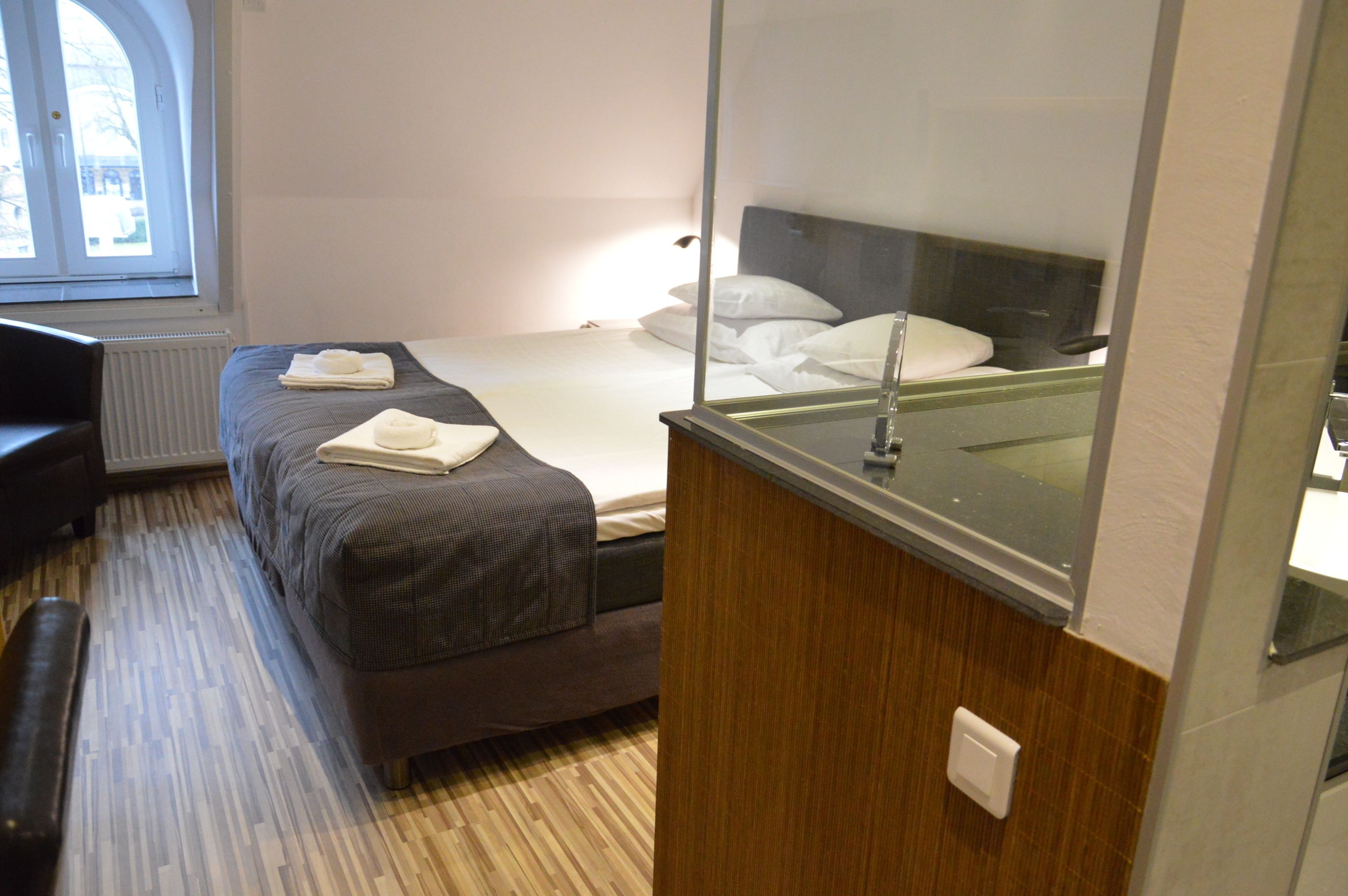 A hotel room with a bed, a small desk, a chair, and a window.