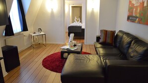 Un dormitorio tipo loft moderno con techo inclinado, un sofá de cuero negro, una alfombra roja y una pequeña mesa con una lámpara.